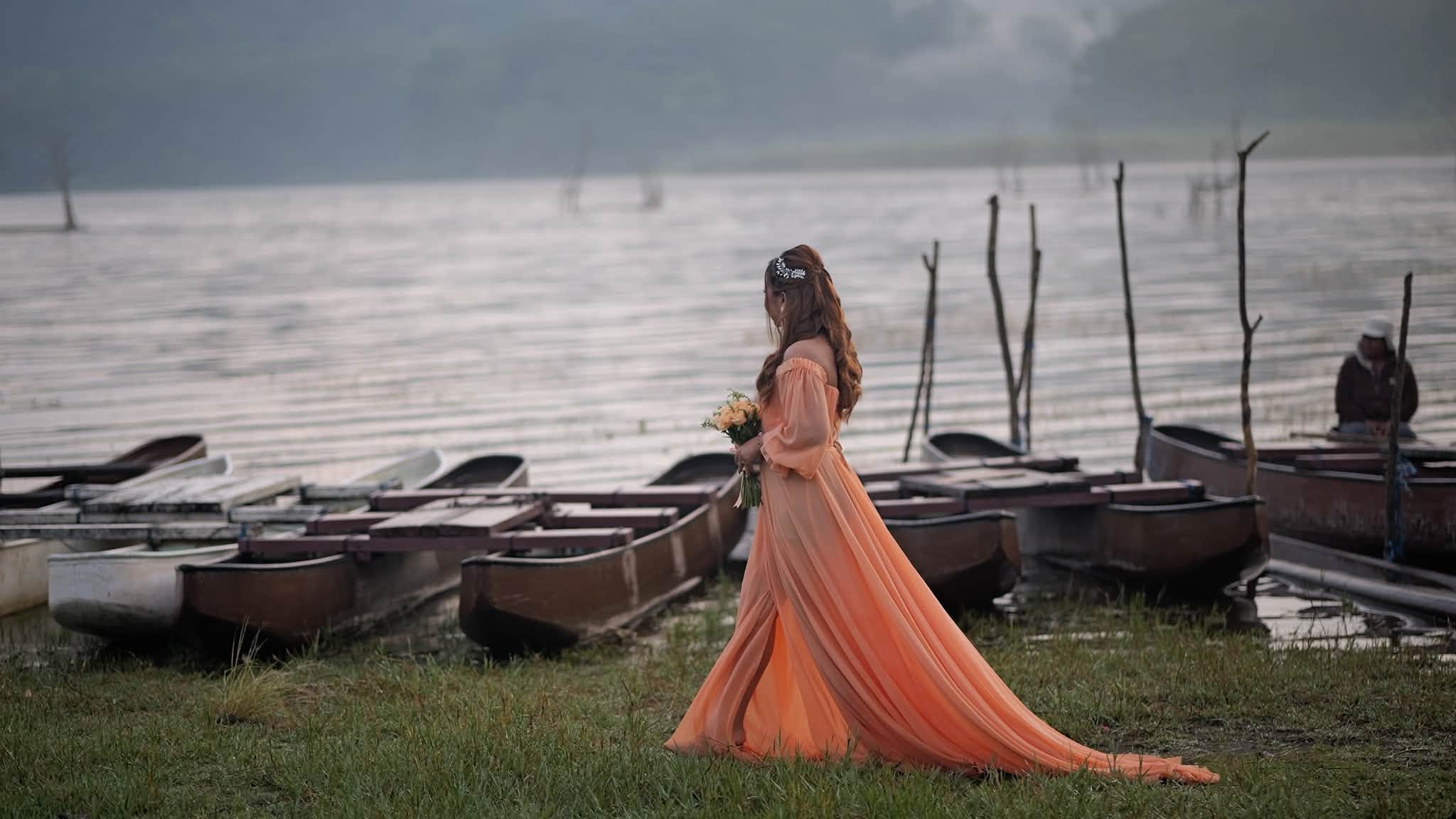 A woman in a gown by a lake with boats